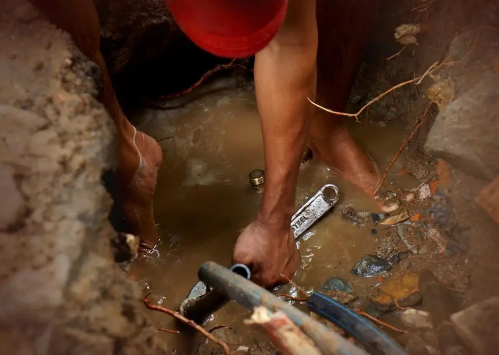 Plumber working outdoors in a pit repairing pipes.